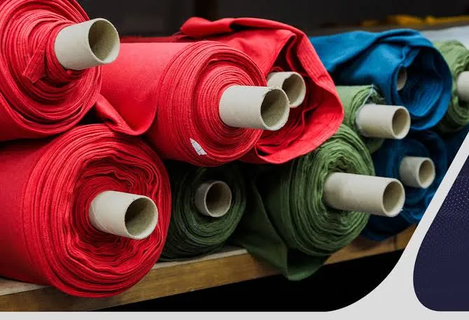 Rolls of red, green, and blue fabric stacked on a mill shelf