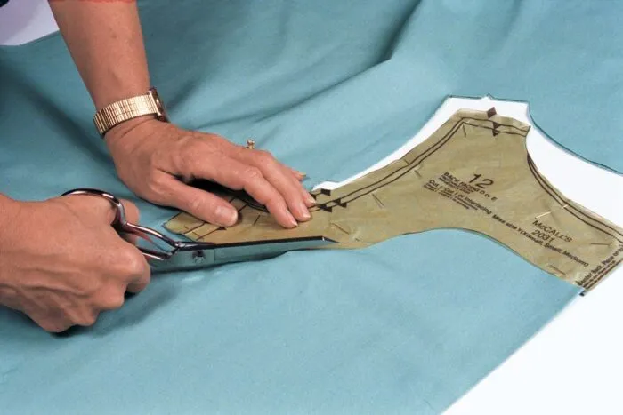 Cutting a paper pattern piece from teal fabric with shears