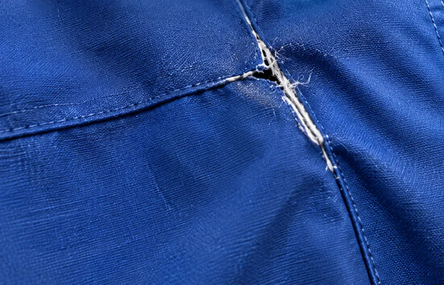A burst seam in blue fabric with split stitching and frayed thread