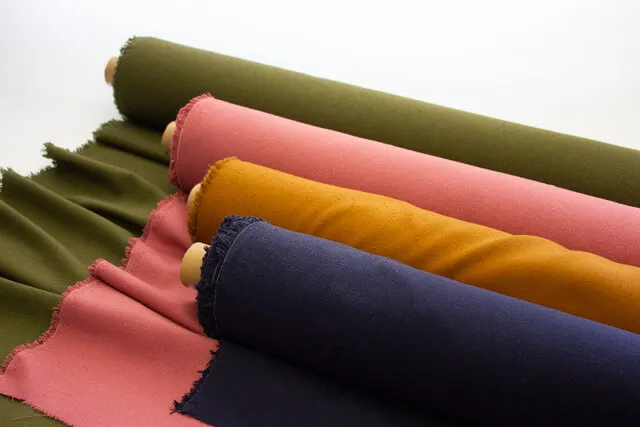 Fabric rolls in olive, rose, mustard, and navy staged for specification approval