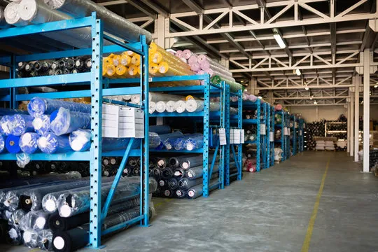 Custom workwear raw material routing: fabric rolls staged on warehouse racking before release to the cutting room