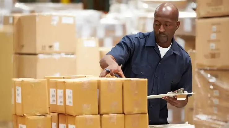 Warehouse staff checking a receiving clipboard against labeled uniform cartons during a site rollout