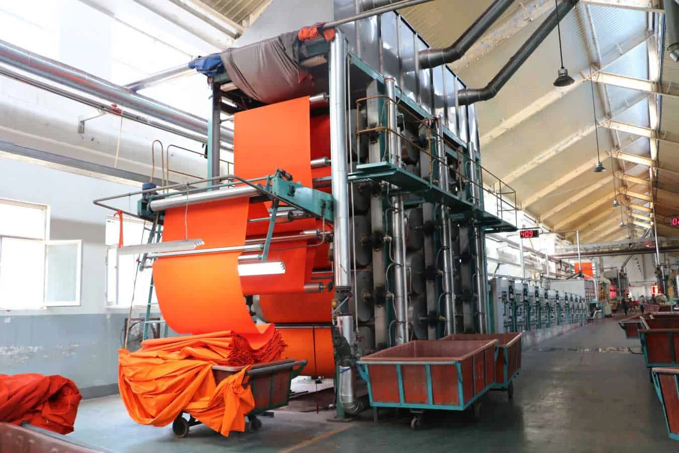 Orange fabric running through a dyehouse finishing line, with transport carts below