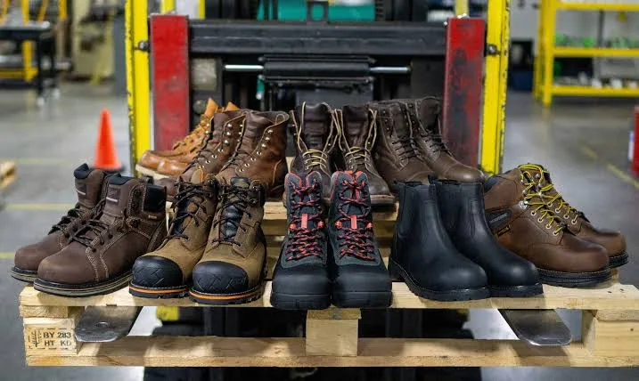 Work boots from several brands lined up on a pallet in a warehouse