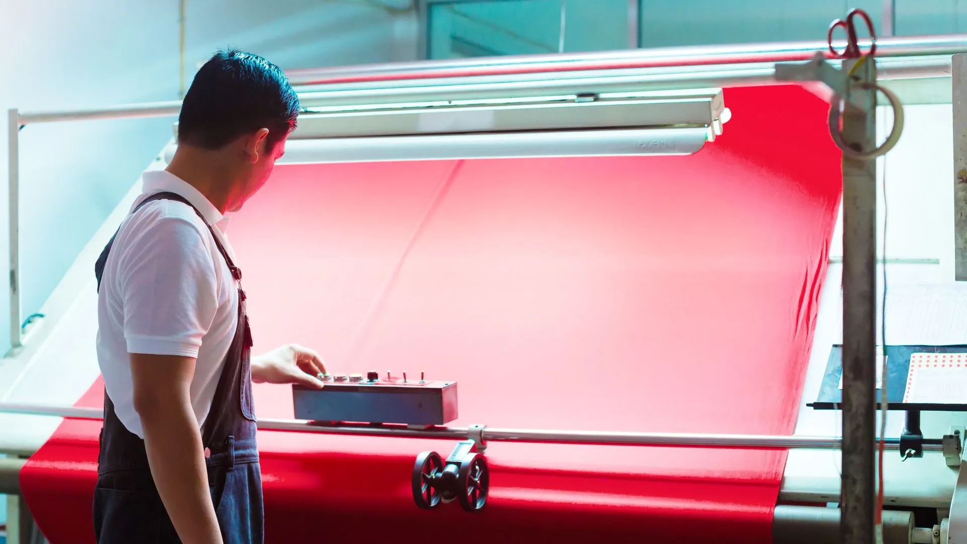 Production worker guiding a red fabric roll through a spreading machine to measure per-size fabric demand before accepting an MOQ